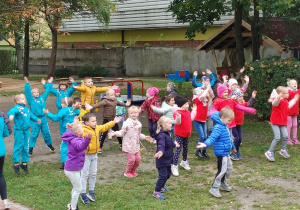 grupa dzieci na podwórku przedszkolnym, wykonują ćwiczenia gimnastyczne